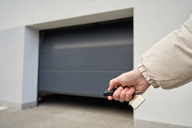 Hand holding remote and keys in front of closed garage door at residential building. Concept of home access and property security